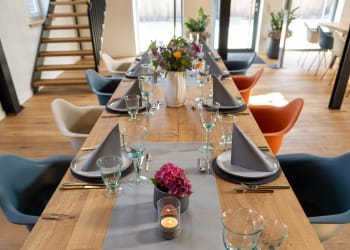 Schön gedeckter Tisch mit Servietten, Tellern, Besteck und Geschirr. Als Dekoration sind Blumen und Kerzen zu sehen.